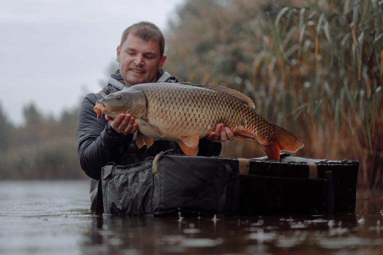 Ein Mann in einer schwarzen Lederjacke hält einen großen, gelben Fisch in seinen Händen in Wasser.